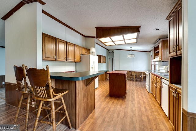 kitchen with a center island, hanging light fixtures, ornamental molding, a kitchen breakfast bar, and white appliances