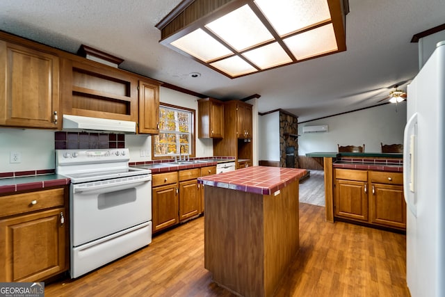 kitchen with a center island, tile counters, white appliances, and light hardwood / wood-style floors