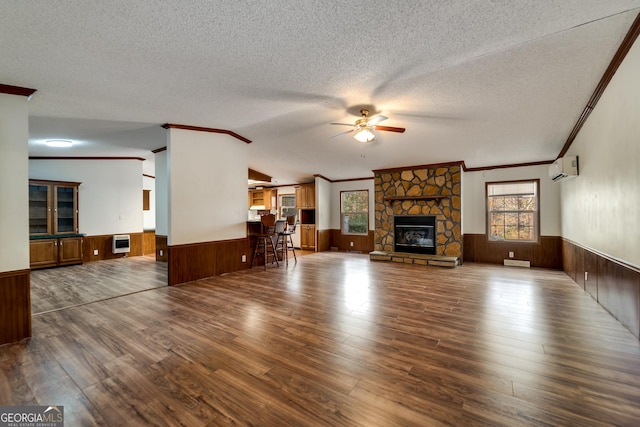 unfurnished living room with ceiling fan, hardwood / wood-style floors, a wall mounted air conditioner, a textured ceiling, and a stone fireplace