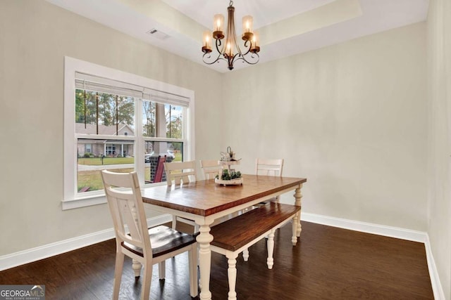 dining space featuring an inviting chandelier, a tray ceiling, and dark hardwood / wood-style floors