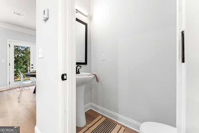 bathroom with toilet, wood-type flooring, and crown molding