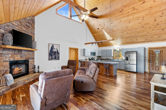 living room with dark hardwood / wood-style flooring, ceiling fan, high vaulted ceiling, wooden ceiling, and a fireplace