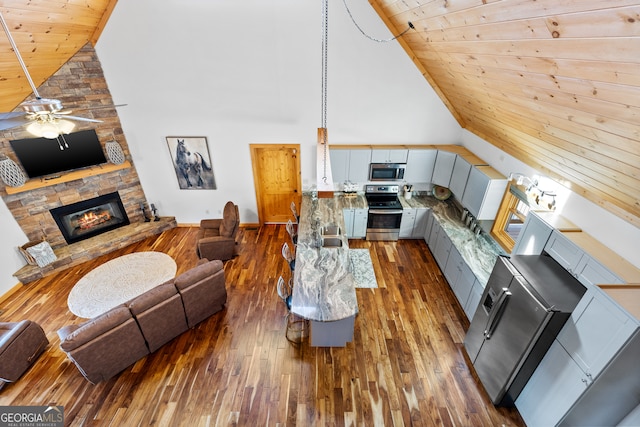 living room featuring dark wood-type flooring, high vaulted ceiling, a stone fireplace, ceiling fan, and wood ceiling