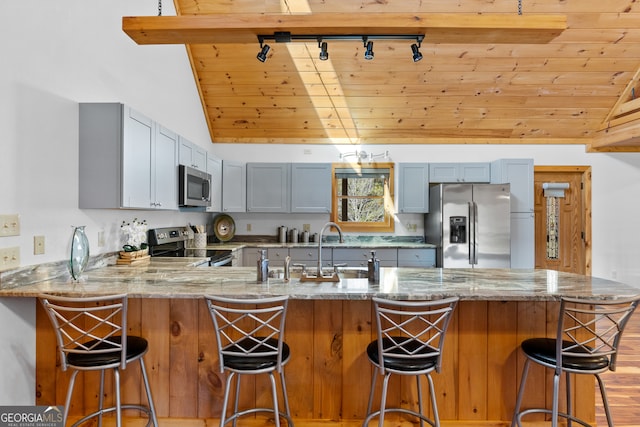 kitchen with lofted ceiling with beams, kitchen peninsula, appliances with stainless steel finishes, light hardwood / wood-style floors, and wood ceiling