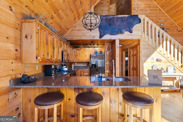 kitchen featuring kitchen peninsula, fridge with ice dispenser, stainless steel stove, light hardwood / wood-style flooring, and wooden walls