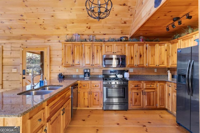 kitchen with hanging light fixtures, light wood-type flooring, wood walls, black appliances, and sink