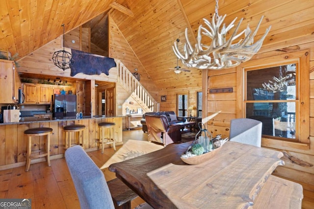 dining space featuring wooden ceiling, ceiling fan with notable chandelier, light hardwood / wood-style floors, and wood walls