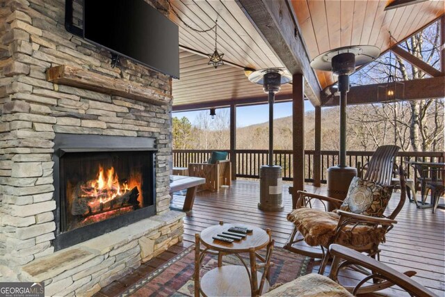 sunroom featuring beamed ceiling, wood ceiling, a mountain view, and an outdoor stone fireplace