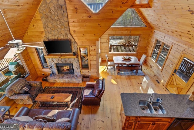 living room with ceiling fan, hardwood / wood-style flooring, high vaulted ceiling, a fireplace, and wooden walls