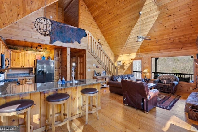 kitchen featuring wood walls, light hardwood / wood-style flooring, high vaulted ceiling, and black fridge