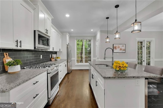 kitchen with appliances with stainless steel finishes, a kitchen island with sink, hanging light fixtures, light stone countertops, and white cabinets