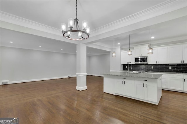 kitchen with light stone countertops, white cabinetry, tasteful backsplash, hanging light fixtures, and a center island with sink