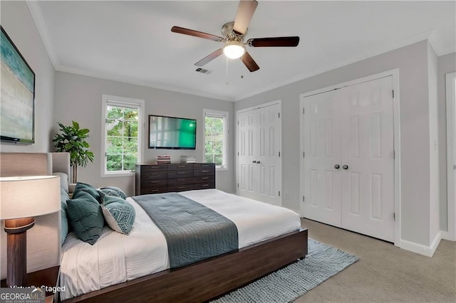 bedroom with ceiling fan, light carpet, crown molding, and multiple closets