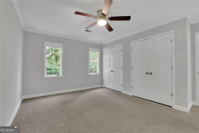 unfurnished bedroom with ceiling fan, crown molding, light colored carpet, and multiple closets