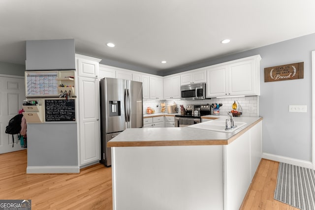 kitchen with light hardwood / wood-style flooring, kitchen peninsula, backsplash, white cabinetry, and appliances with stainless steel finishes