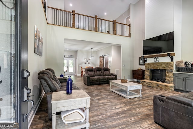 living room featuring a stone fireplace, dark wood-type flooring, and a high ceiling