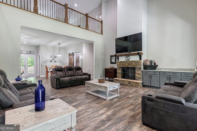 living room with a towering ceiling, dark wood-type flooring, a stone fireplace, and a barn door