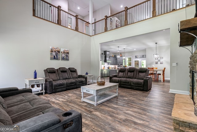 living room with dark hardwood / wood-style flooring, a stone fireplace, an inviting chandelier, and a high ceiling