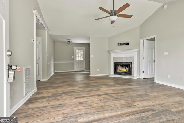 unfurnished living room with ceiling fan, high vaulted ceiling, a tile fireplace, and dark hardwood / wood-style floors