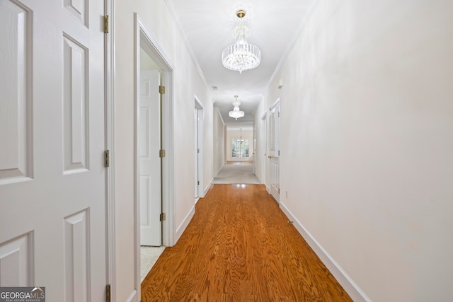 corridor with ornamental molding, light hardwood / wood-style flooring, and an inviting chandelier