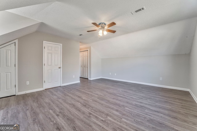 additional living space featuring a textured ceiling, visible vents, baseboards, ceiling fan, and wood finished floors