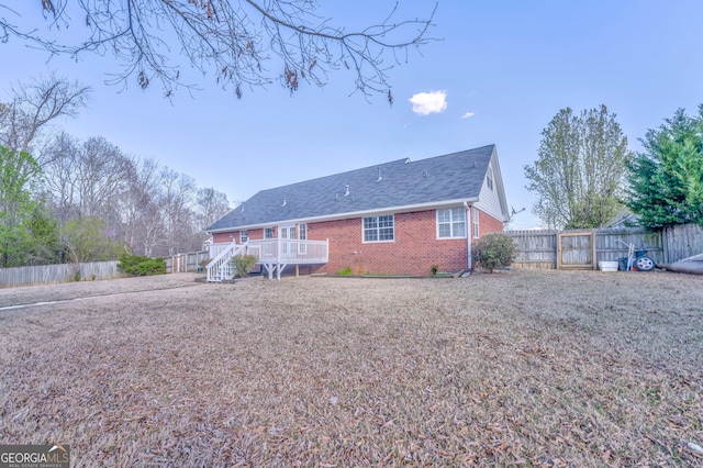 rear view of property featuring brick siding, a wooden deck, and a fenced backyard