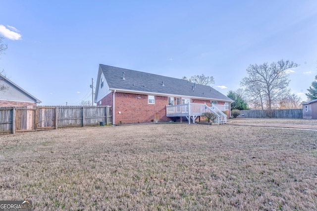 rear view of property featuring a lawn, brick siding, a fenced backyard, and a wooden deck