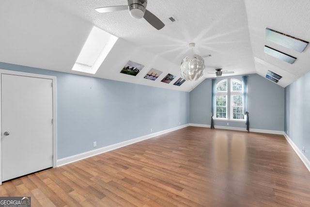 additional living space with a textured ceiling, vaulted ceiling with skylight, wood-type flooring, and ceiling fan