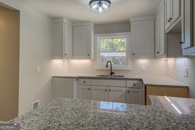 kitchen featuring sink, light stone counters, and white cabinetry