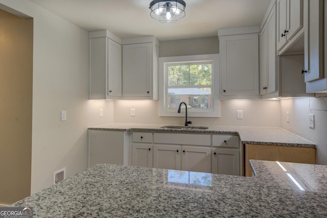 kitchen with visible vents, light stone counters, a sink, and white cabinetry