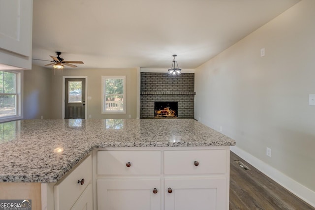 kitchen featuring a brick fireplace, a wealth of natural light, light stone counters, and white cabinetry