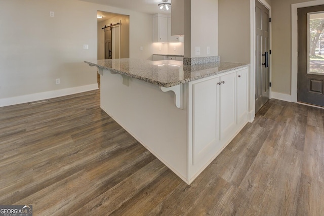 kitchen with a barn door, white cabinets, dark wood finished floors, a breakfast bar, and a peninsula