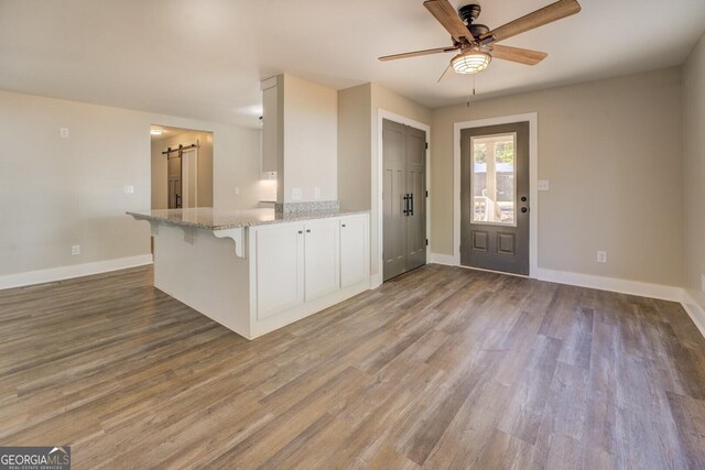 kitchen with white cabinetry, kitchen peninsula, light stone counters, light hardwood / wood-style flooring, and a barn door