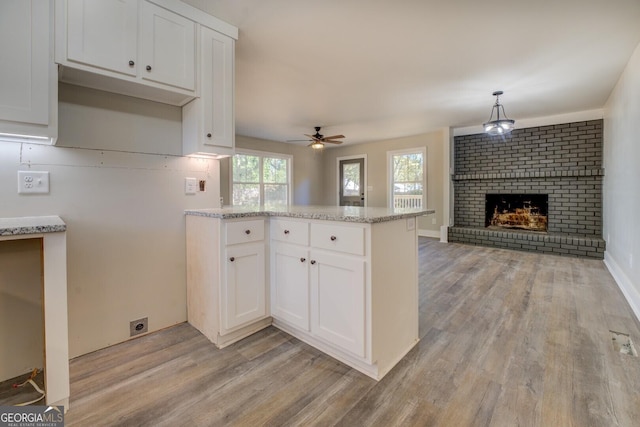 kitchen with white cabinets, a brick fireplace, hanging light fixtures, kitchen peninsula, and ceiling fan