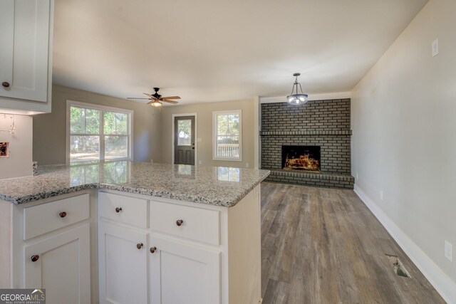 kitchen with hardwood / wood-style flooring, a brick fireplace, ceiling fan, white cabinets, and light stone counters