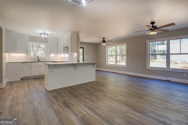 kitchen with ceiling fan, light stone countertops, white cabinetry, and a kitchen island