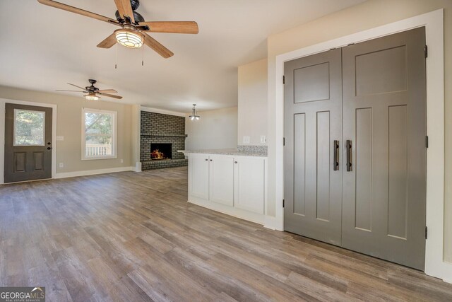 unfurnished living room featuring ceiling fan, light wood-type flooring, and a fireplace