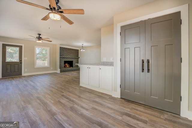 unfurnished living room with a brick fireplace, ceiling fan, baseboards, and wood finished floors