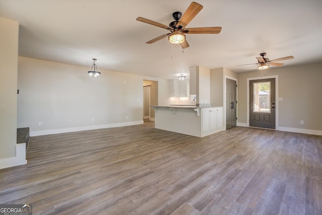 unfurnished living room featuring ceiling fan, wood finished floors, and baseboards