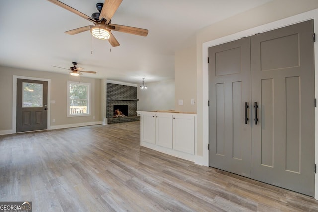 unfurnished living room featuring a brick fireplace, light wood-style flooring, and baseboards