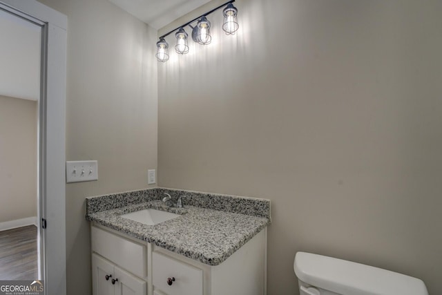 half bath featuring baseboards, vanity, toilet, and wood finished floors