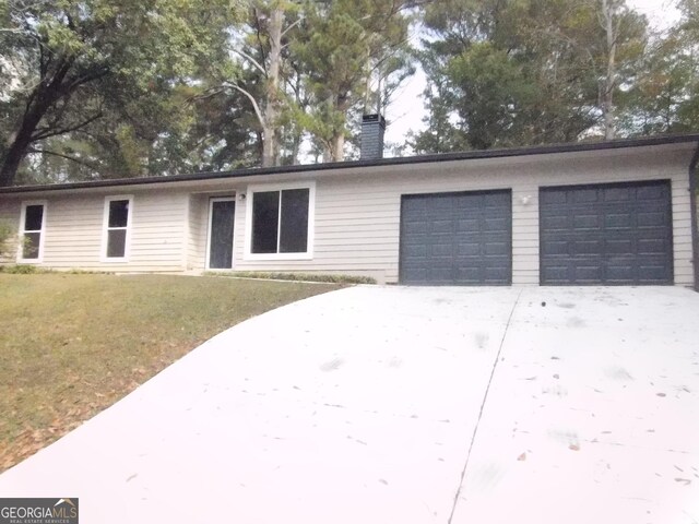 single story home featuring an attached garage, concrete driveway, a chimney, and a front yard