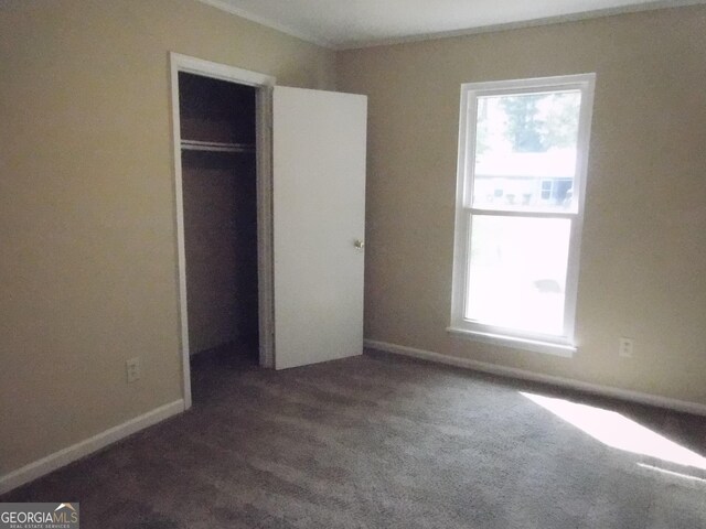 unfurnished bedroom featuring a closet, dark colored carpet, and baseboards