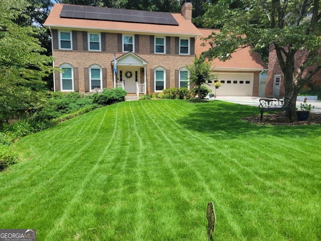 colonial home with a front yard, solar panels, and a garage