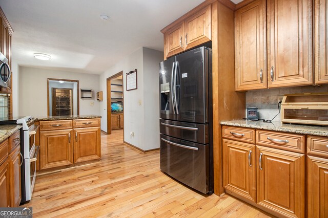 kitchen featuring light stone countertops, appliances with stainless steel finishes, light hardwood / wood-style flooring, and backsplash