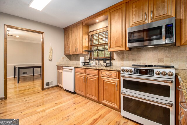 kitchen with sink, appliances with stainless steel finishes, light stone counters, and light wood-type flooring