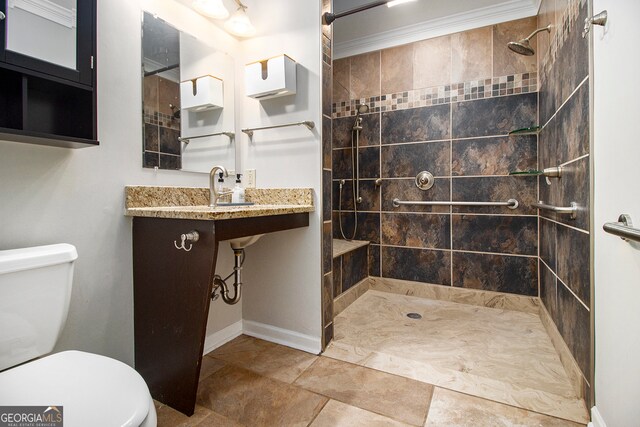 bathroom with a tile shower, toilet, ornamental molding, and sink