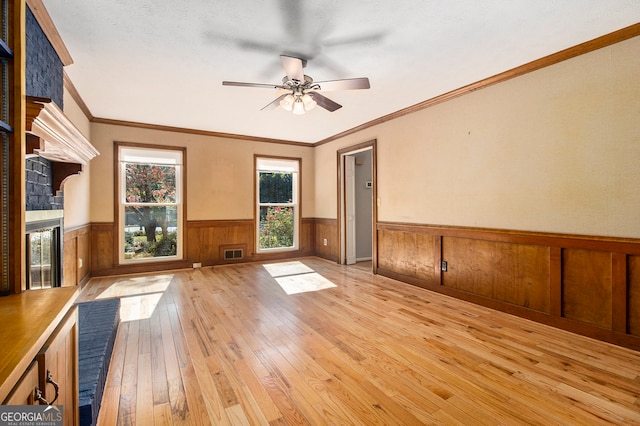 unfurnished living room featuring light wood-type flooring, a fireplace, a textured ceiling, ceiling fan, and crown molding