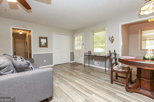 living area featuring light wood finished floors, visible vents, ceiling fan, baseboards, and attic access