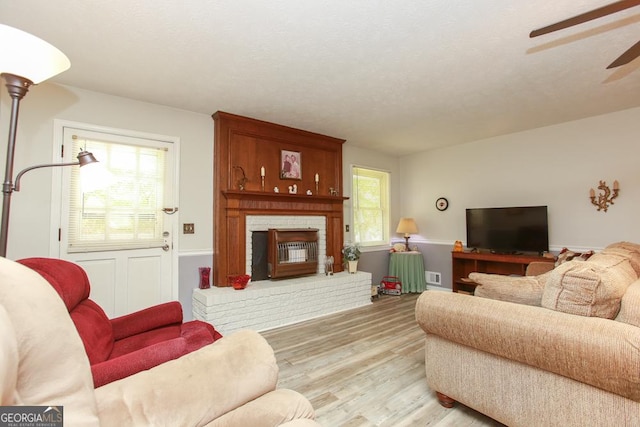 living area with light wood finished floors, visible vents, ceiling fan, a fireplace, and a textured ceiling